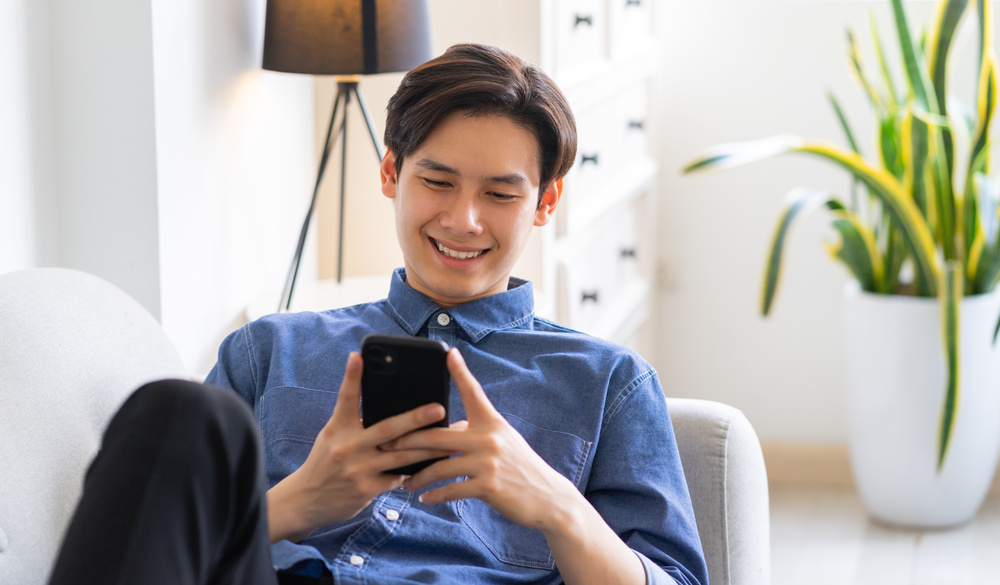 Young,Asian,Man,Lying,On,Sofa,And,Using,Phone